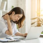 デスクワーク女性と肩こり 「PC作業で肩を押さえてつらそうにしている女性」