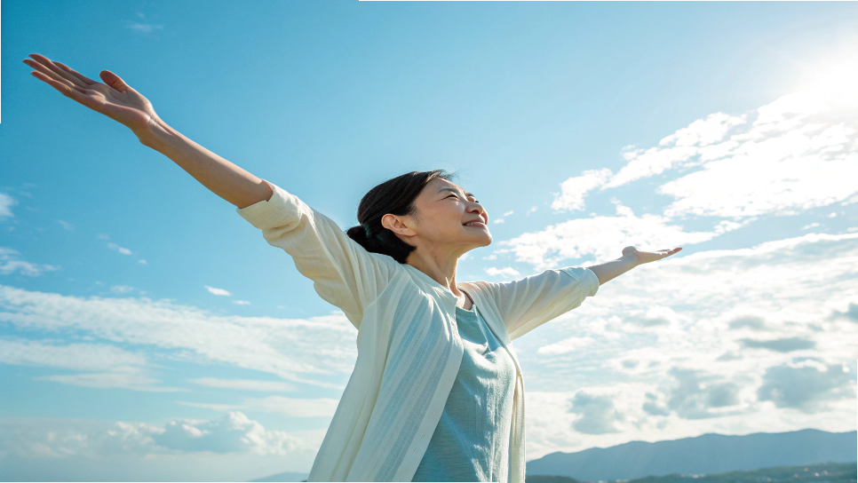 青空の下で深呼吸をする女性。胸を広げてリフレッシュ。