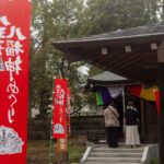八王子七福神めぐりの赤いのぼり旗と、お堂の前で静かに手を合わせる参拝客の後ろ姿
