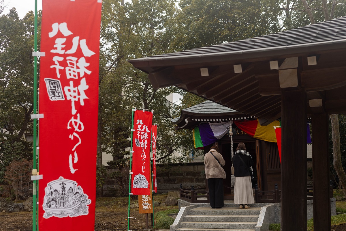 八王子は七福神ならぬ“八”福神?新年の開運散歩と、歩き疲れた足のケア 1 八王子七福神めぐりの赤いのぼり旗と、お堂の前で静かに手を合わせる参拝客の後ろ姿