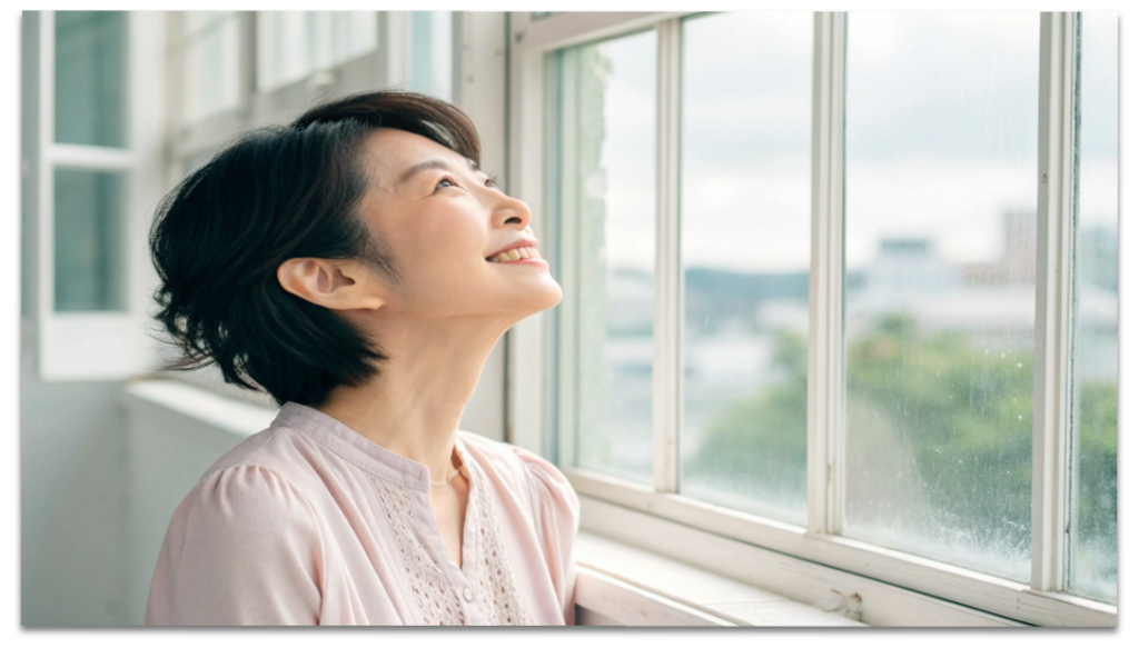 経絡と骨格調整で首こりが解消し、スッキリとした表情で窓の外を見る女性の写真。
